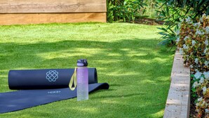 A yoga mat and a water bottle on a well-maintained lawn with a wooden planter and flowering plants. - Can Masarol: Views, Pool & BBQ - Platja d'Aro (Castell-Platja d'Aro)