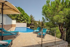Área de piscina com espreguiçadeiras e um muro de pedra.