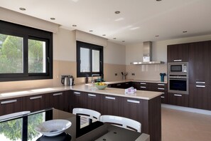 Eine moderne Küche mit dunklen Holzschränken, einer zentralen Kochinsel mit Spüle und integrierten Geräten, darunter eine Mikrowelle und ein Backofen.