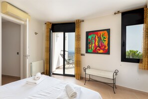 Ein Hotelzimmer mit Bett, Sitzbank, Fenster mit Vorhängen, Heizkörper und einem Gemälde.