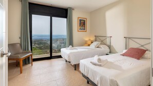 A hotel room with two beds, a chair, a large window with a view, and a poster on the wall. - Can Masarol: Views, Pool & BBQ - Platja d'Aro (Castell-Platja d'Aro)