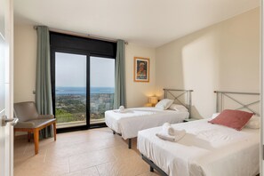 Ein Hotelzimmer mit zwei Betten, einem Sessel, einem großen Fenster mit Blick und einem Bild an der Wand.