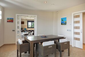 Ein stilvoller Essbereich mit einem dunklen Holztisch und passenden Stühlen, im Hintergrund eine Küche und Kunstwerke an den Wänden.