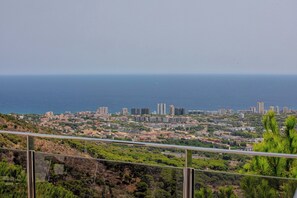 Eine Küstenstadt mit einer Mischung aus Wohn- und Hochhäusern, freier Sicht auf das Meer und hügeligem Gelände im Vordergrund.