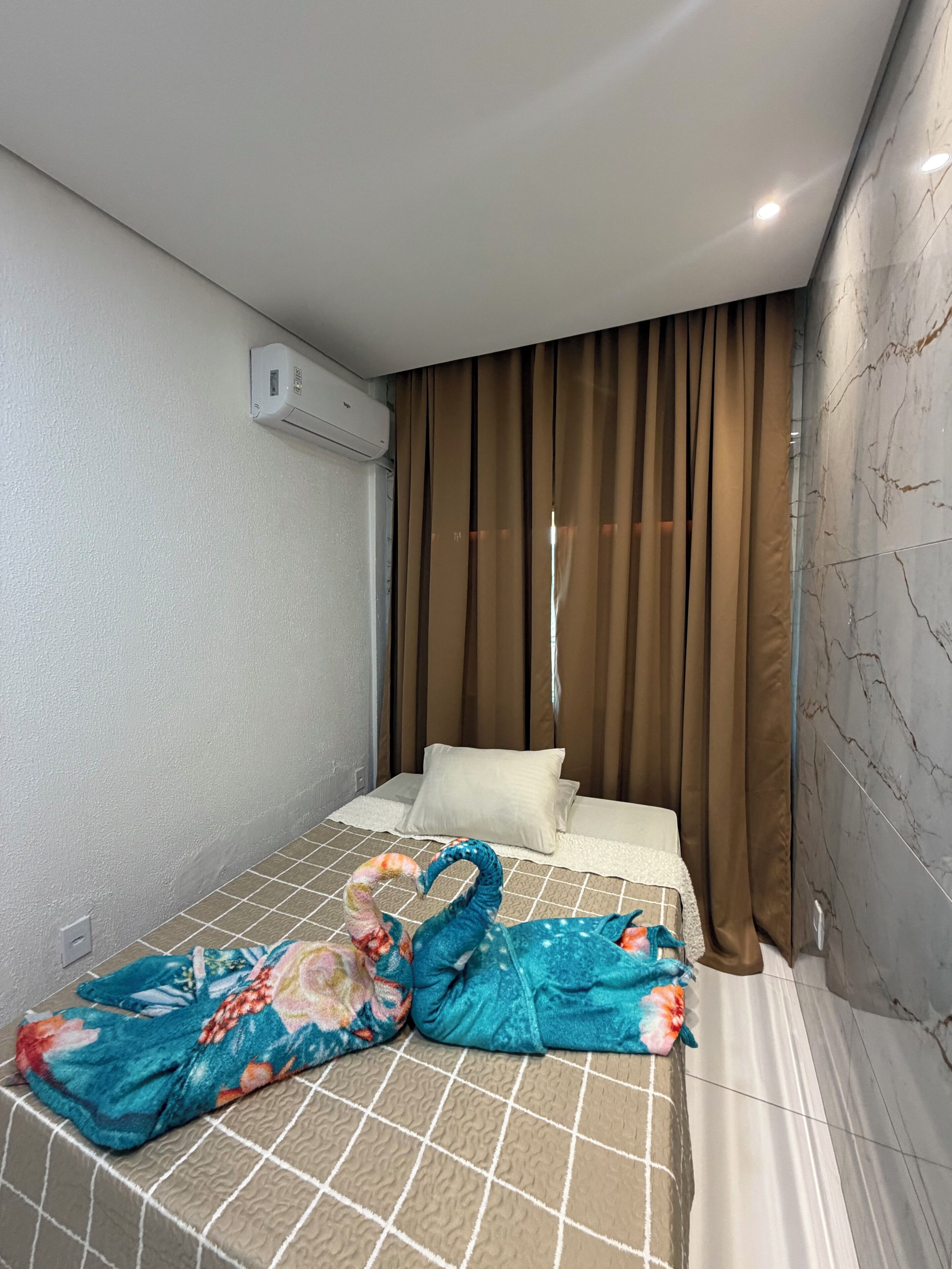 Habitación de hotel con cama, almohada, manta y aire acondicionado en la pared.