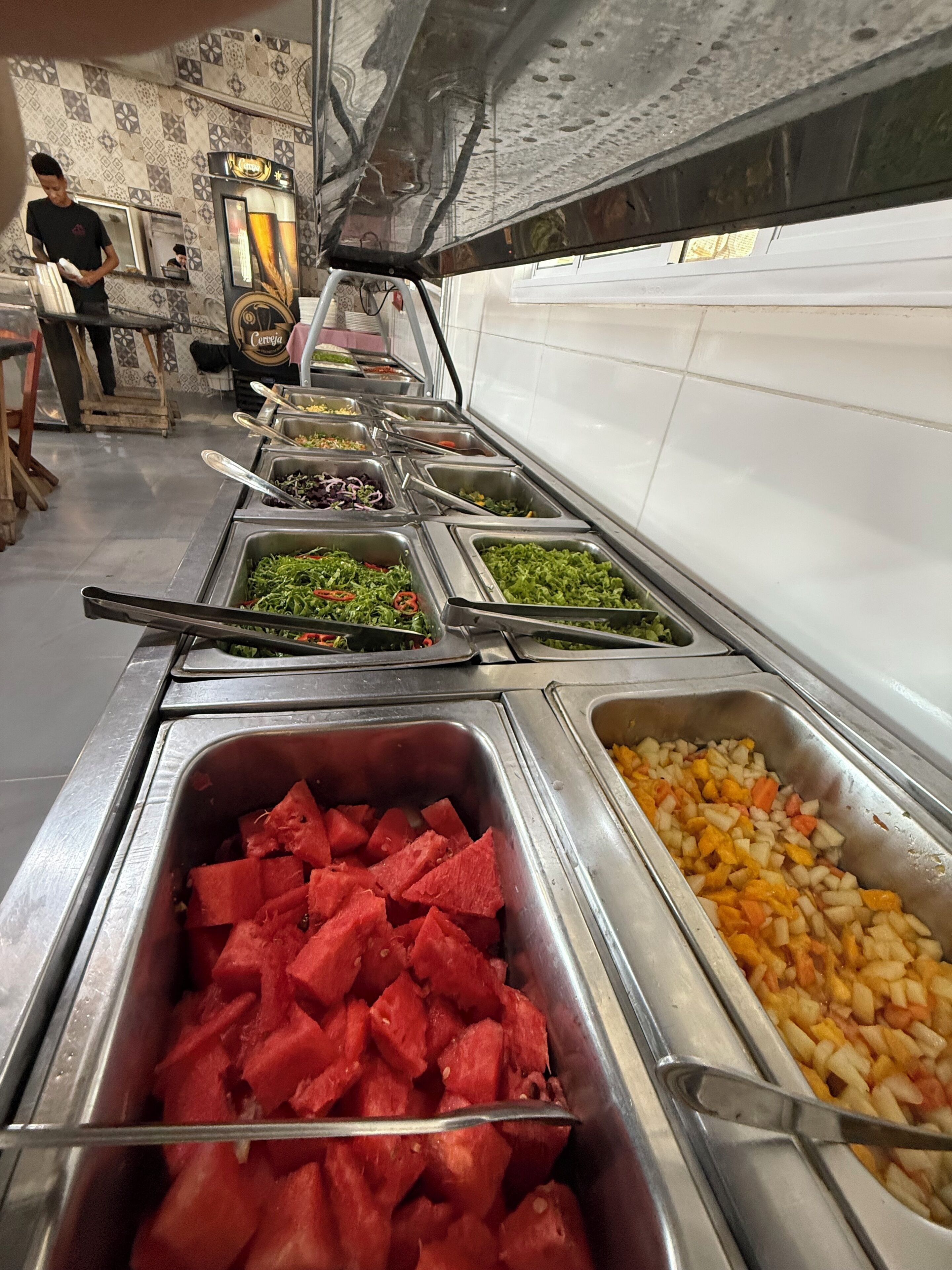 Una barra de buffet con diversas opciones de comida, incluyendo sandía, verduras mixtas y otros platos.
