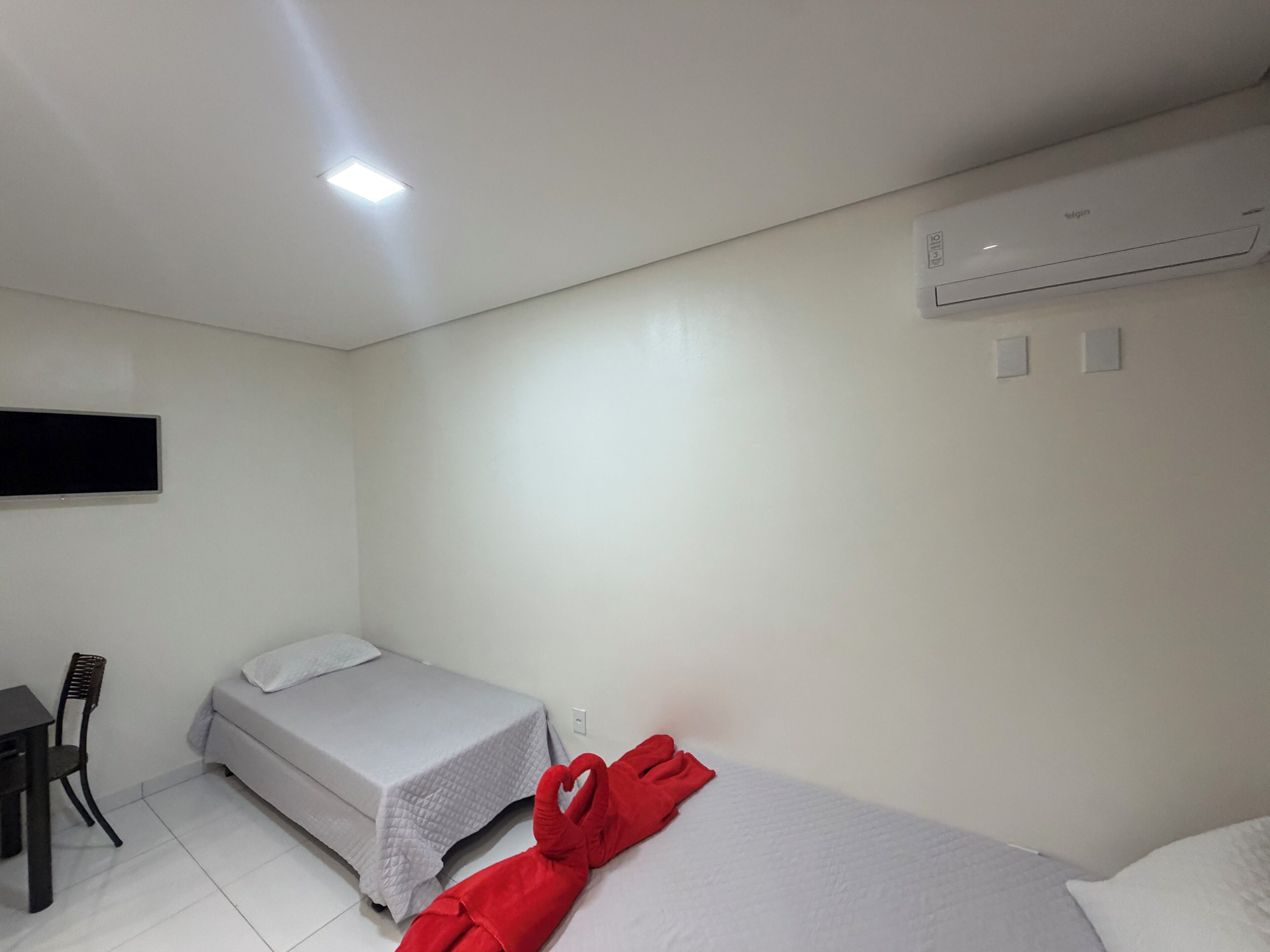 A single-bed room with a bed, a chair, a desk, and a wall-mounted air conditioner.