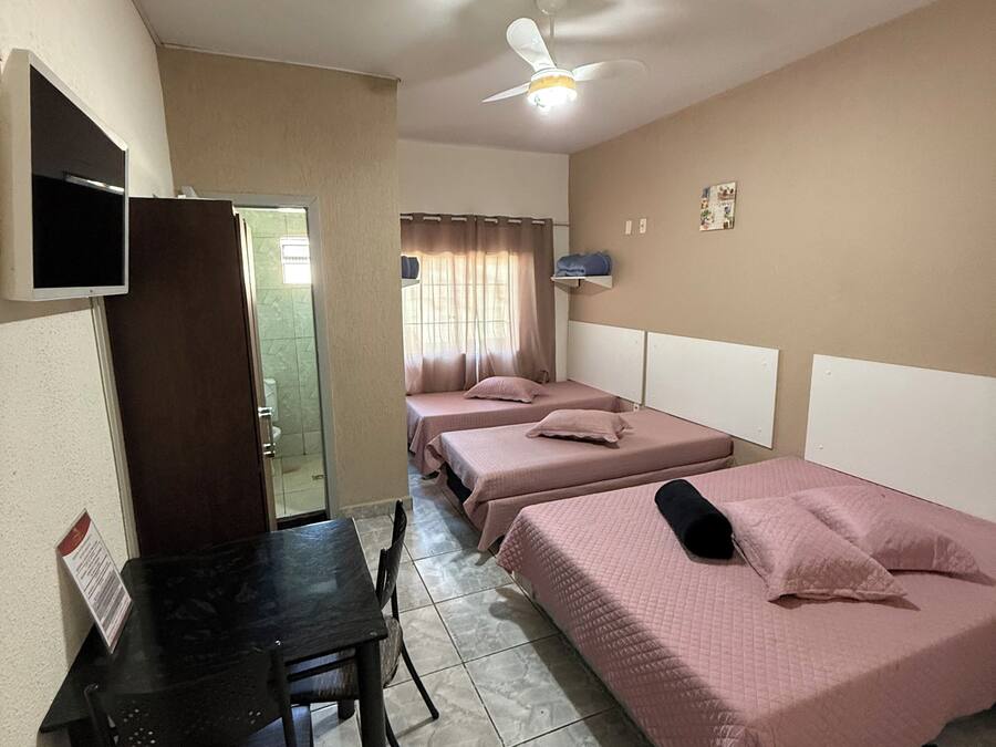 Una habitación con dos camas, un escritorio, una silla, un televisor y un ventilador de techo.