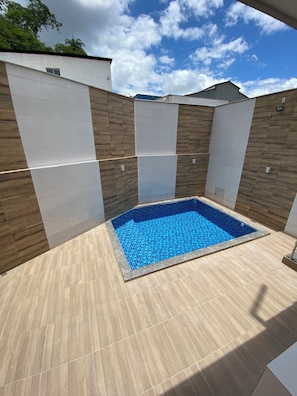 Ein rechteckiger Pool mit blau gefliestem Innenraum, umgeben von Wänden aus weißer Verkleidung und Holzpaneelen.