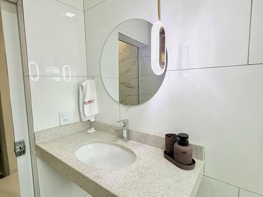 Ein modernes Badezimmer mit einer Granitplatte, einem runden Spiegel, einem Handtuchspender und einem Toilettenpapierhalter.