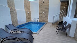 A swimming pool with lounge chairs, a tiled floor, and a staircase leading to an upper level.