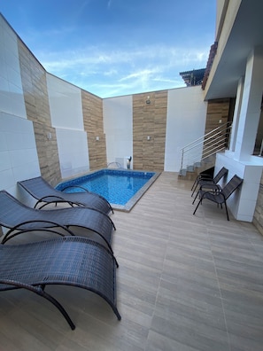 Una piscina con sillas de descanso, suelo de baldosas y una escalera que sube a un nivel superior.