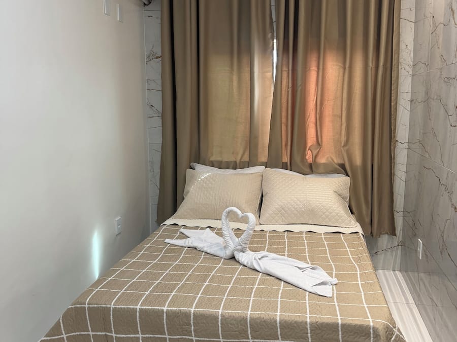 A hotel room with a bed, beige curtains, a white air conditioning unit, and a marble-patterned wall.