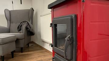 A red wood-burning stove in a room with a grey sofa and a wooden floor.