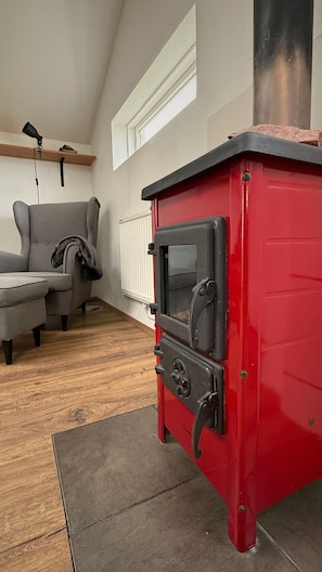 A red wood-burning stove in a room with a grey sofa and a wooden floor.