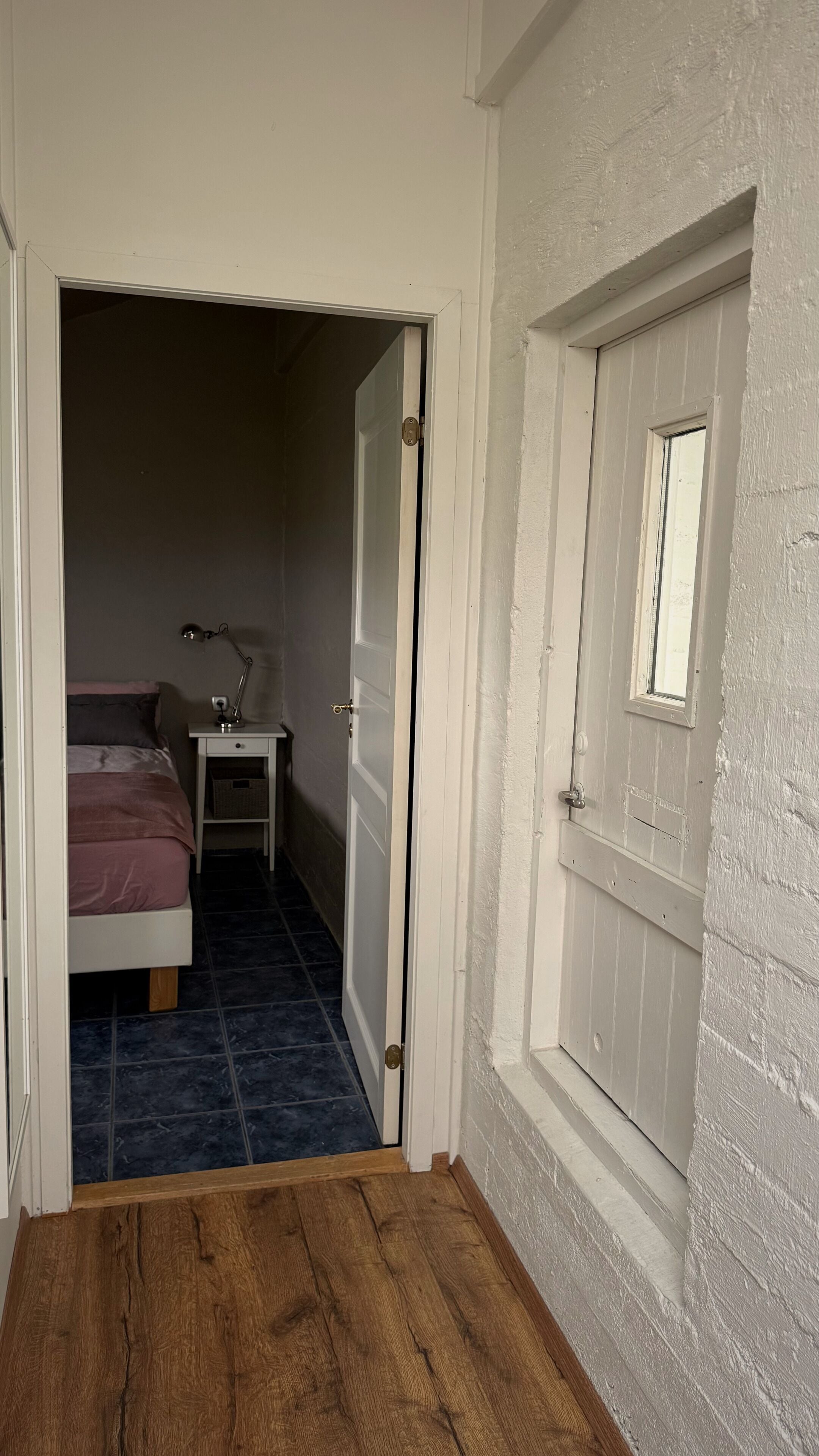 Un pasillo estrecho con piso de madera que conduce a un dormitorio con cama y mesita de noche.
