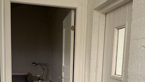 Um corredor estreito com piso de madeira que dá para um quarto com cama e mesa de cabeceira.