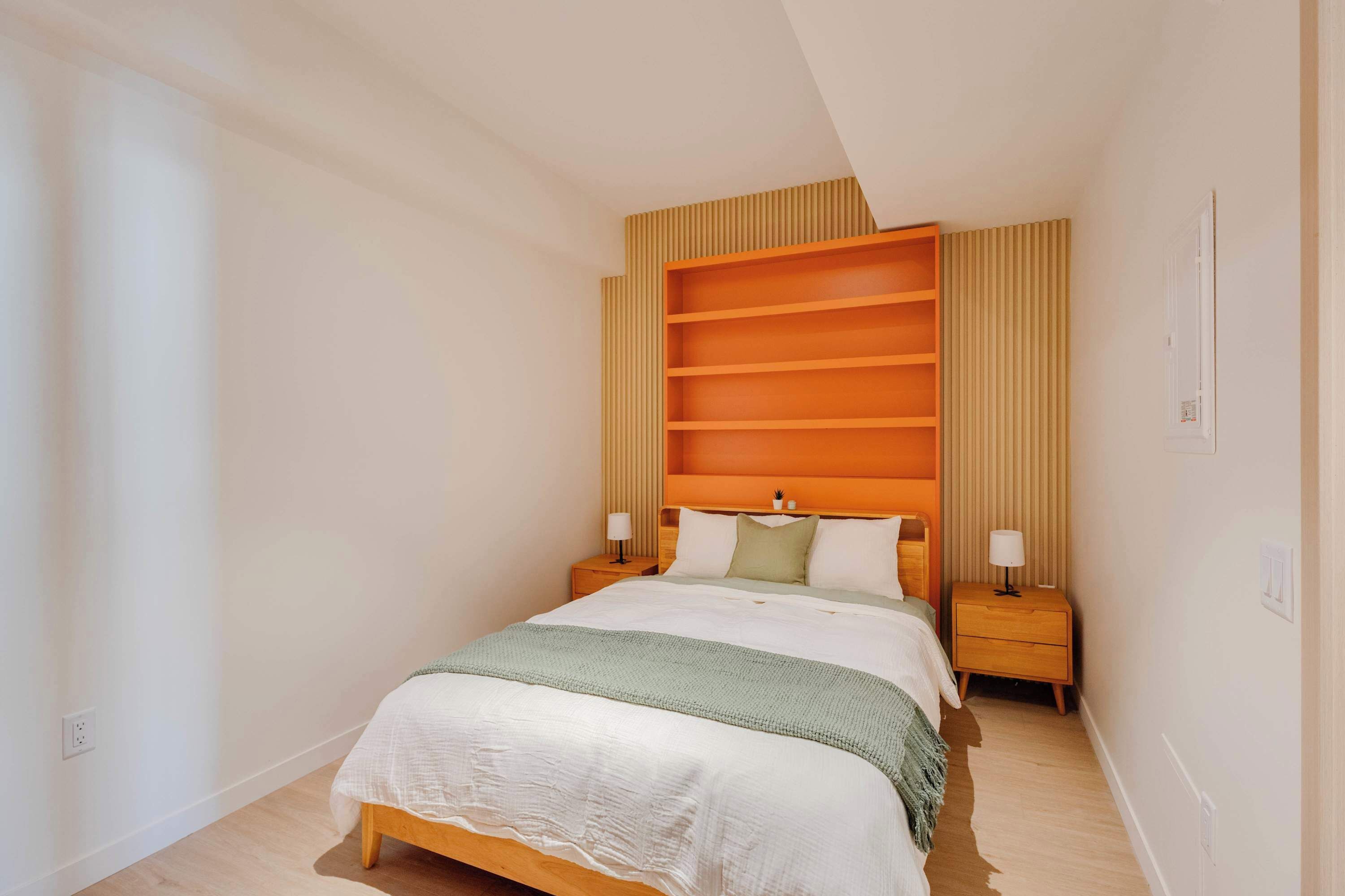 A modern bedroom with a bed, bedside tables, and a built-in shelving unit.