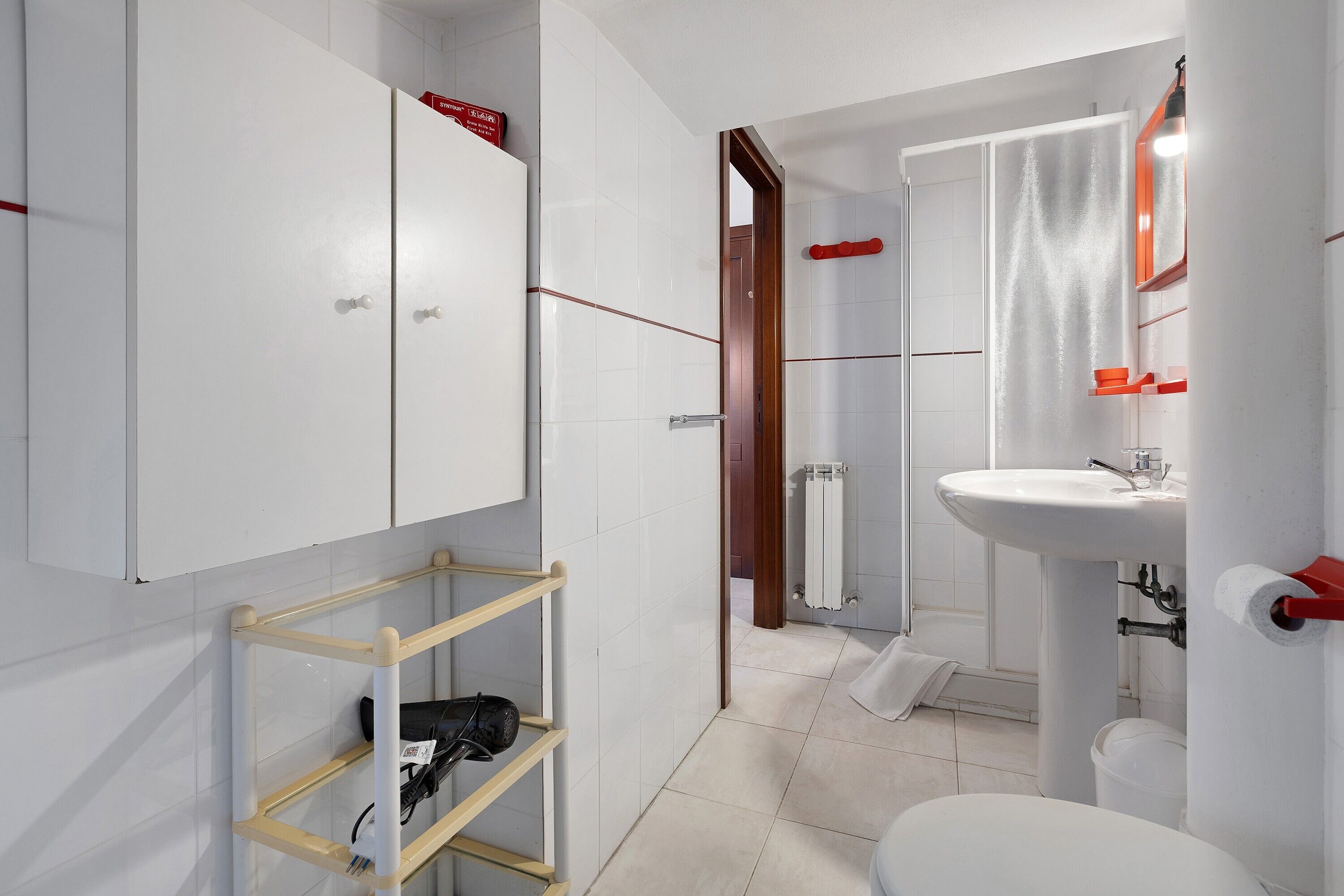 Ein modernes Badezimmer mit Toilette, Waschbecken und Dusche. Ein Handtuchhalter und ein Ablagebereich mit einem Fön sind vorhanden.