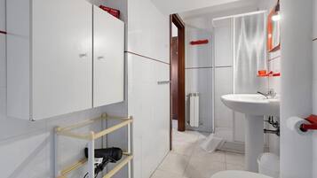 Ein modernes Badezimmer mit Toilette, Waschbecken und Dusche. Ein Handtuchhalter und ein Ablagebereich mit einem Fön sind vorhanden.