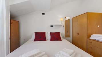 Habitación de hotel con cama, dos almohadas, mesita de noche, lámpara, armario y espejo.