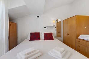 Habitación de hotel con cama, dos almohadas, mesita de noche, lámpara, armario y espejo.