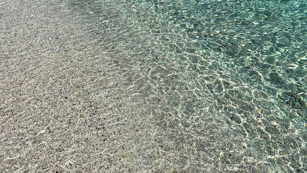 Uma praia calma com pedras visíveis e mar tranquilo.