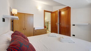 Quarto de hotel com cama, guarda-roupa, espelho e prateleira.