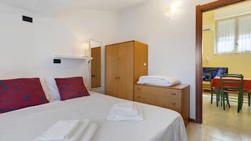 A bedroom with a bed, a wardrobe, a desk with a chair, and a television.