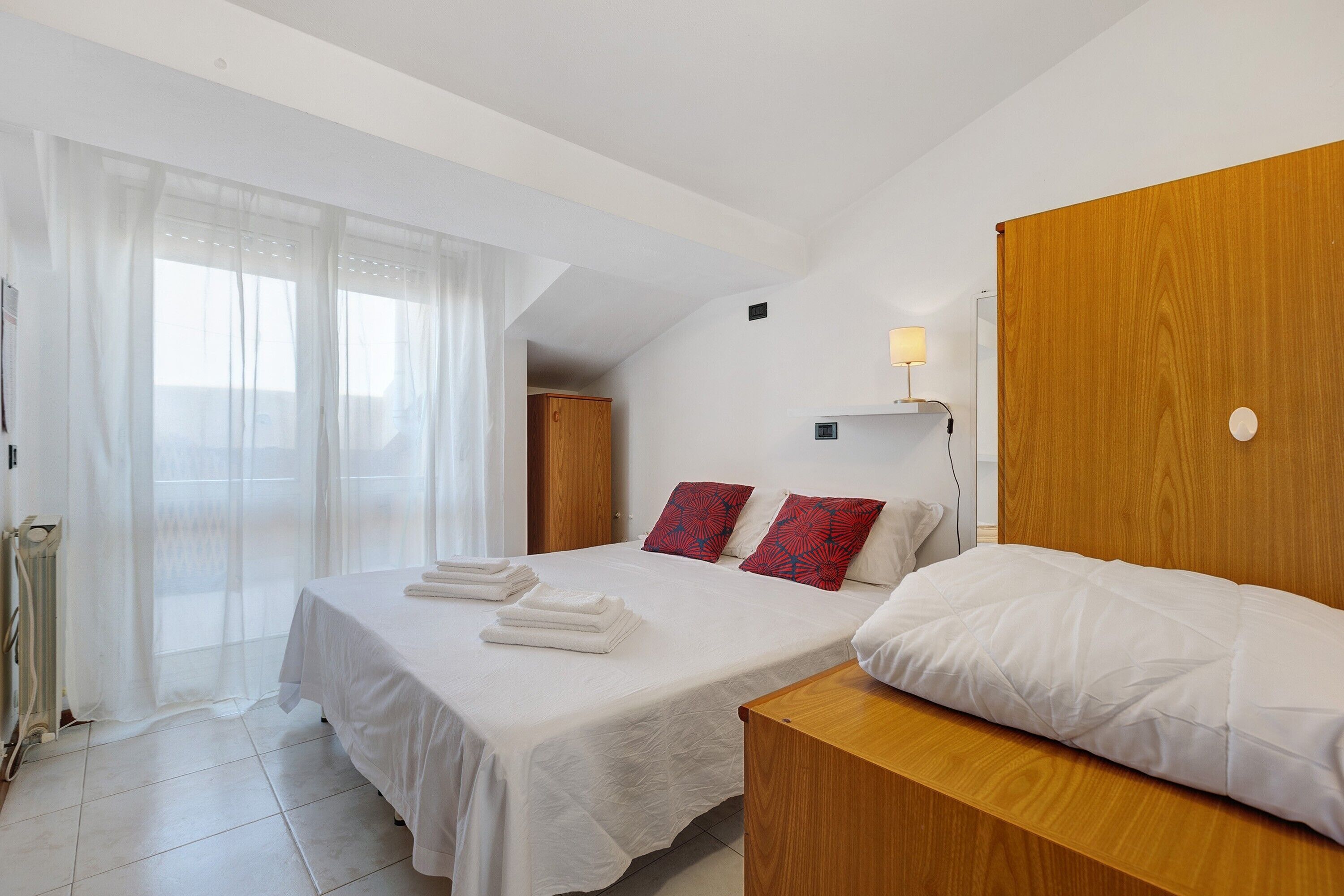 Habitación de hotel con cama, cabecera de madera, mesita de noche, lámpara y ventana con cortinas.