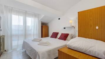 Habitación de hotel con cama, cabecera de madera, mesita de noche, lámpara y ventana con cortinas.