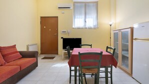 Um espaço compacto com sofá, mesa de jantar e cadeiras, televisão, frigorífico e janela com cortinas.