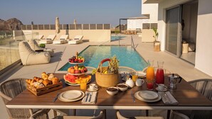 Ein Frühstückstisch am Pool mit Stühlen und Blick auf Pool und Meer.