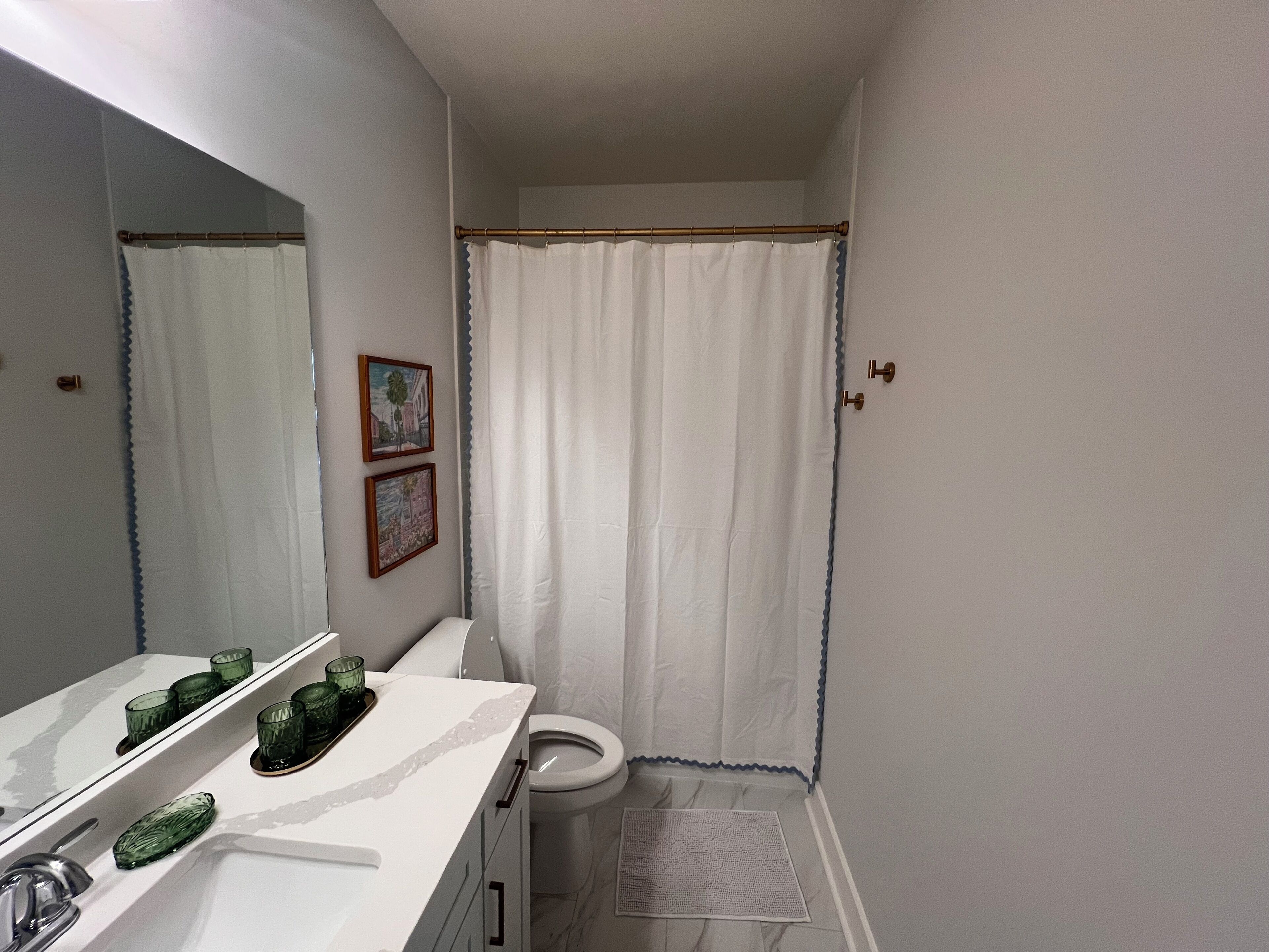 Ein Badezimmer mit Toilette, Duschvorhang, Waschbecken mit Spiegel und einem kleinen Teppich.