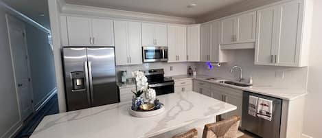 A modern kitchen with white cabinetry, stainless steel appliances, and a marble island with bar stools.