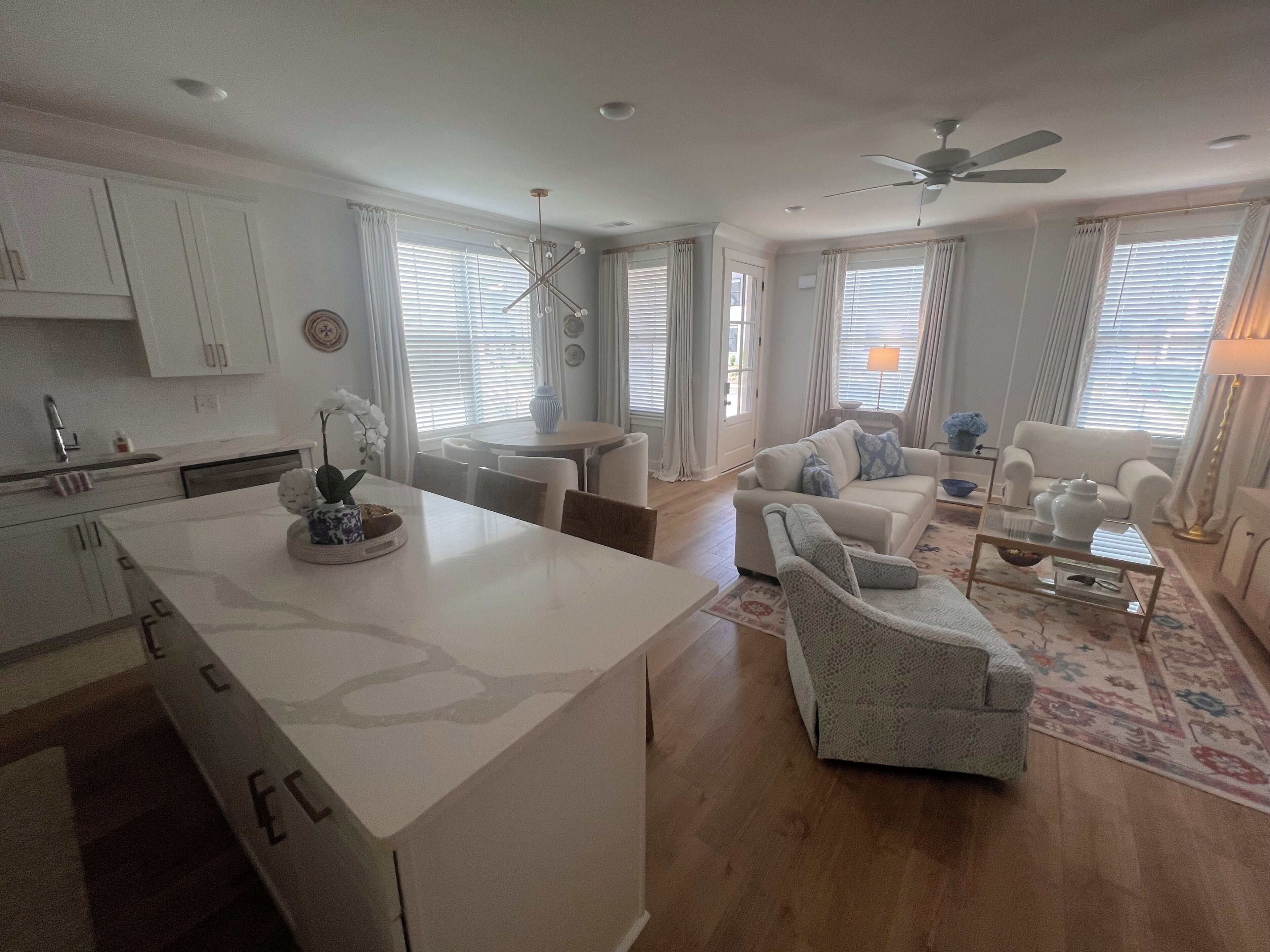 A modern living room with a sofa, armchairs, a coffee table, and a dining area with a kitchen in the background.