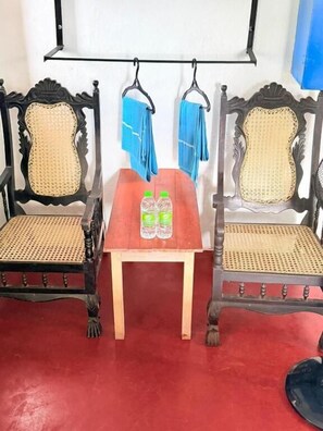 Una habitación con dos sillas ornamentadas de asiento tejido, una pequeña mesa de madera con dos botellas y una alfombra roja.