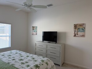 A bedroom with a bed, a dresser, a ceiling fan, and two wall-mounted paintings. - Live the Village Dream One Beautiful Day at a Time! (The Villages)