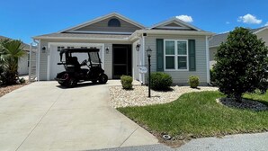 Ein eingeschossiges Haus mit Garage, ein Golfwagen davor und einem gepflegten Rasen.
