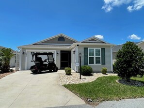 Ein eingeschossiges Haus mit Garage, ein Golfwagen davor und einem gepflegten Rasen.