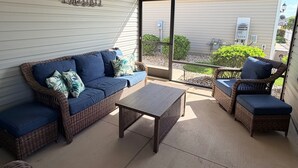 Eine überdachte Terrasse mit Korbmöbeln, einem Deckenventilator und Blick auf den Garten.