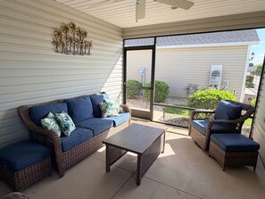 Eine überdachte Terrasse mit Korbmöbeln, einem Deckenventilator und Blick auf den Garten.