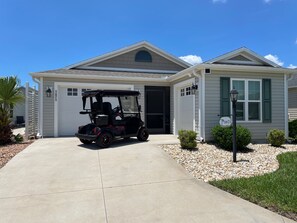 A residential house with a garage, a driveway, and a golf cart parked in front. - Live the Village Dream One Beautiful Day at a Time! (The Villages)