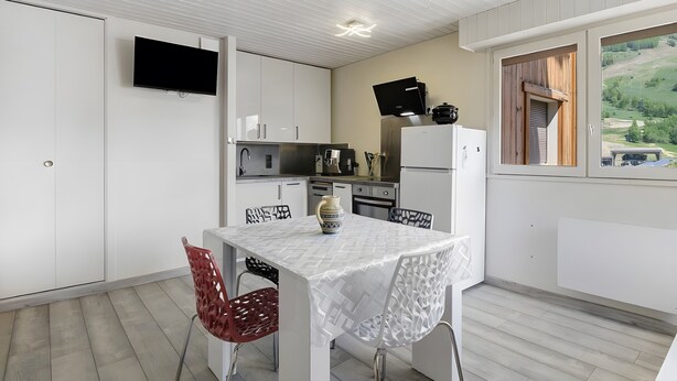 A compact kitchen with white cabinets, a flat-screen TV, and a dining area with a table and chairs. - Apartment “Les Deux Alpes” with Mountain View, Balcony, and Wi-Fi (Les Deux Alpes)