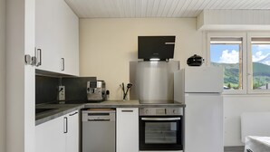 A modern kitchen with white cabinetry, a built-in coffee machine, a stainless steel range hood, and a view of the outdoors through a window. - Apartment “Les Deux Alpes” with Mountain View, Balcony, and Wi-Fi (Les Deux Alpes)