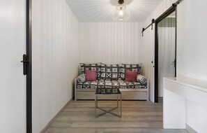 Una habitación estrecha con un sofá estampado, una mesita pequeña y una lámpara en el techo.