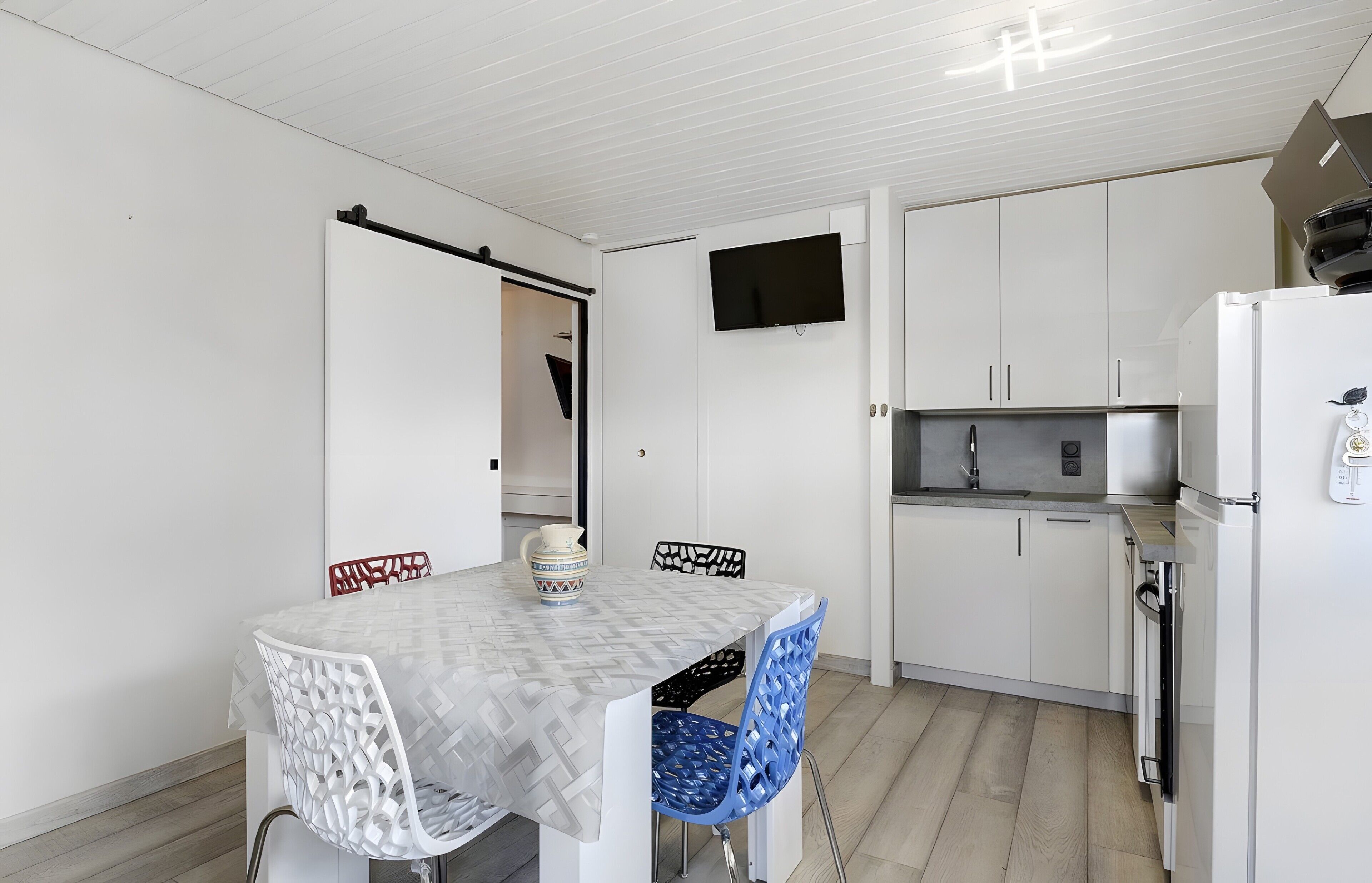 Una cocina compacta con armarios blancos, televisor integrado y refrigerador.