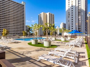 A hotel pool area with lounge chairs, palm trees, and high-rise buildings in the background. - Top-Floor Oceanview Waikiki Banyan| Pool Parking (Honolulu)