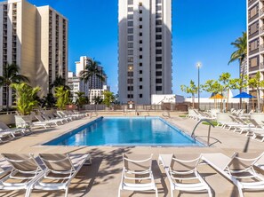A swimming pool with sun loungers and tall buildings in the background. - Waikiki Banyan, Top Floor Oceanview Pool + Parking (Honolulu)