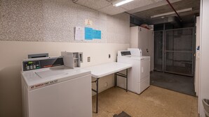 A commercial laundry area with a washing machine, dryer, and a table. - Waikiki Banyan, Top Floor Oceanview Pool + Parking (Honolulu)
